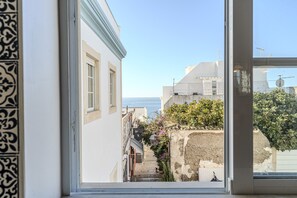 A narrow street with buildings, a clear sky, and the sea in the distance.