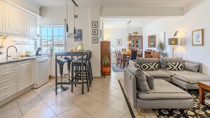 Et moderne køkken med hvide skabe, et spiseområde med bord og stole, en grå modulsofa og en stue med et sofabord.