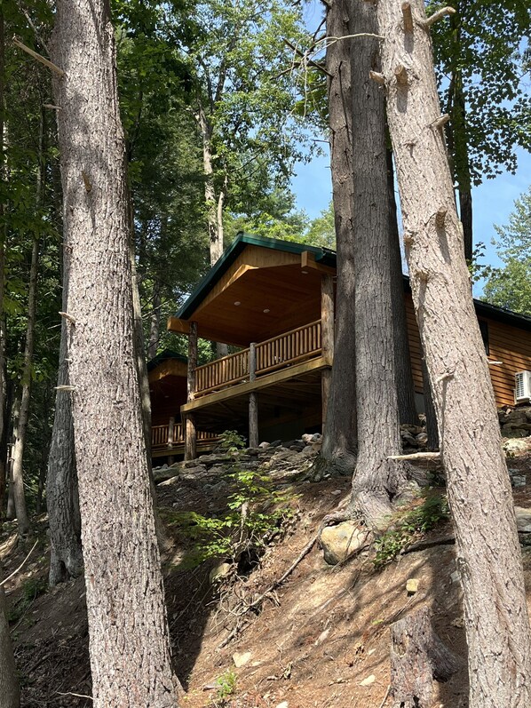 A cabin with a wooden deck and a covered porch, surrounded by tall trees.
