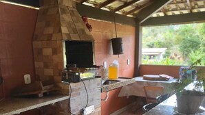 Une cuisine extérieure dotée d’un four en briques, de plans de travail en granit et offrant une vue sur la verdure.