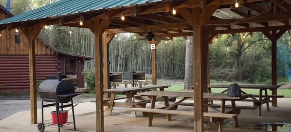 An outdoor wooden pavilion with picnic tables and a barbecue grill.