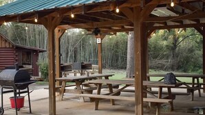 Un pabellón de madera al aire libre con mesas de picnic y una parrilla.