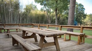 A wooden deck with picnic tables and benches, surrounded by trees. - #18 The LeeSort (Karnack)