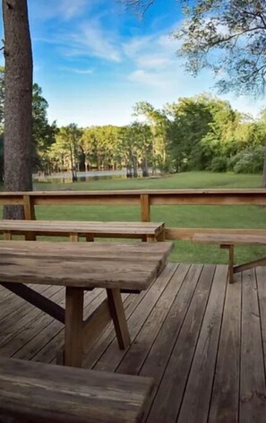 A wooden deck with picnic tables and a view of a grassy field and trees.