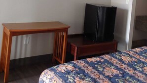 Una habitación con cama, un escritorio de madera, televisión montada en la pared y un refrigerador.