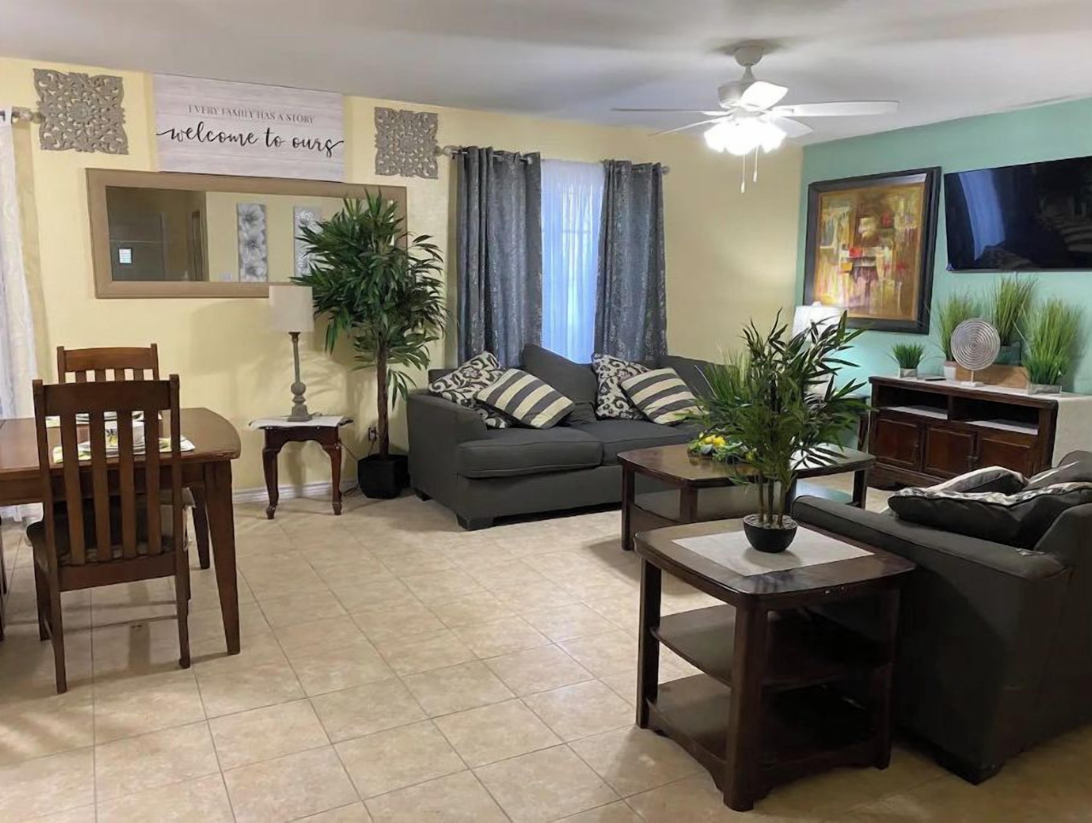 Un salon comprenant un canapé, deux fauteuils, une table basse, un ventilateur de plafond et un téléviseur fixé au mur.