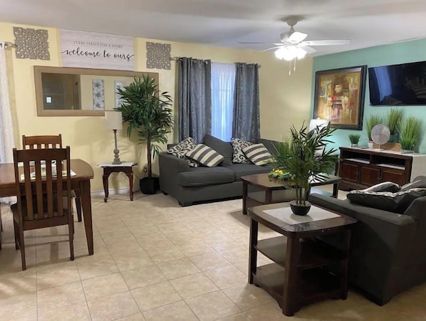 A living room with a sofa, two chairs, a coffee table, a ceiling fan, and a TV on the wall. - Mama’s home (Pharr)