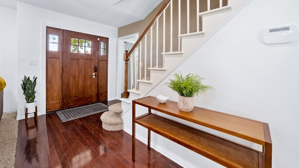 A clean, modern entryway with a wooden door, a white staircase, and a small table with a plant.