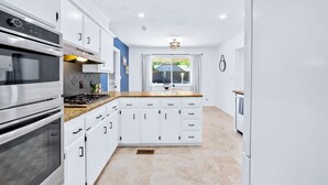 A modern kitchen with white cabinets, stainless steel appliances, and a view of the outdoors through a window.