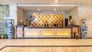 A reception desk with two staff members, a patterned wall, and large vases. - Jingdian Hotel (Nan'an)