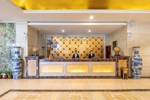 Una mesa de recepción con dos empleados, un papel tapiz decorado y jarrones grandes.