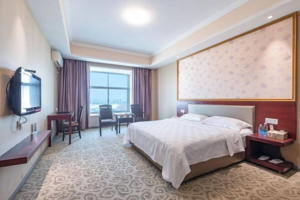 A hotel room with a large bed, a desk with a chair, a television, and a window with curtains.