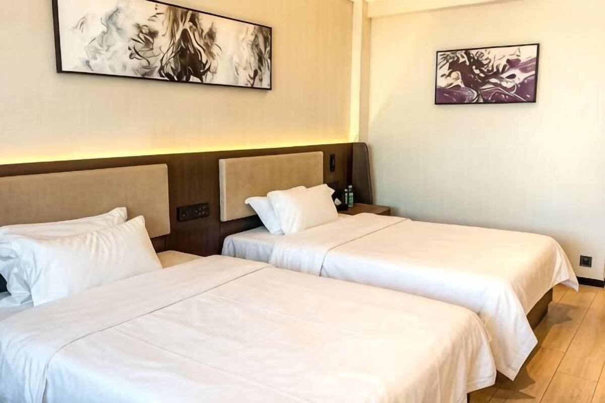 A hotel room with two beds, a nightstand, and artwork on the walls.