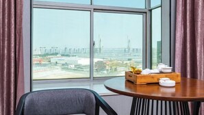 A room with a large window offering a city view, a round wooden table with teapots and a tray, and a modern chair. - Jingdian Hotel (Nan'an)