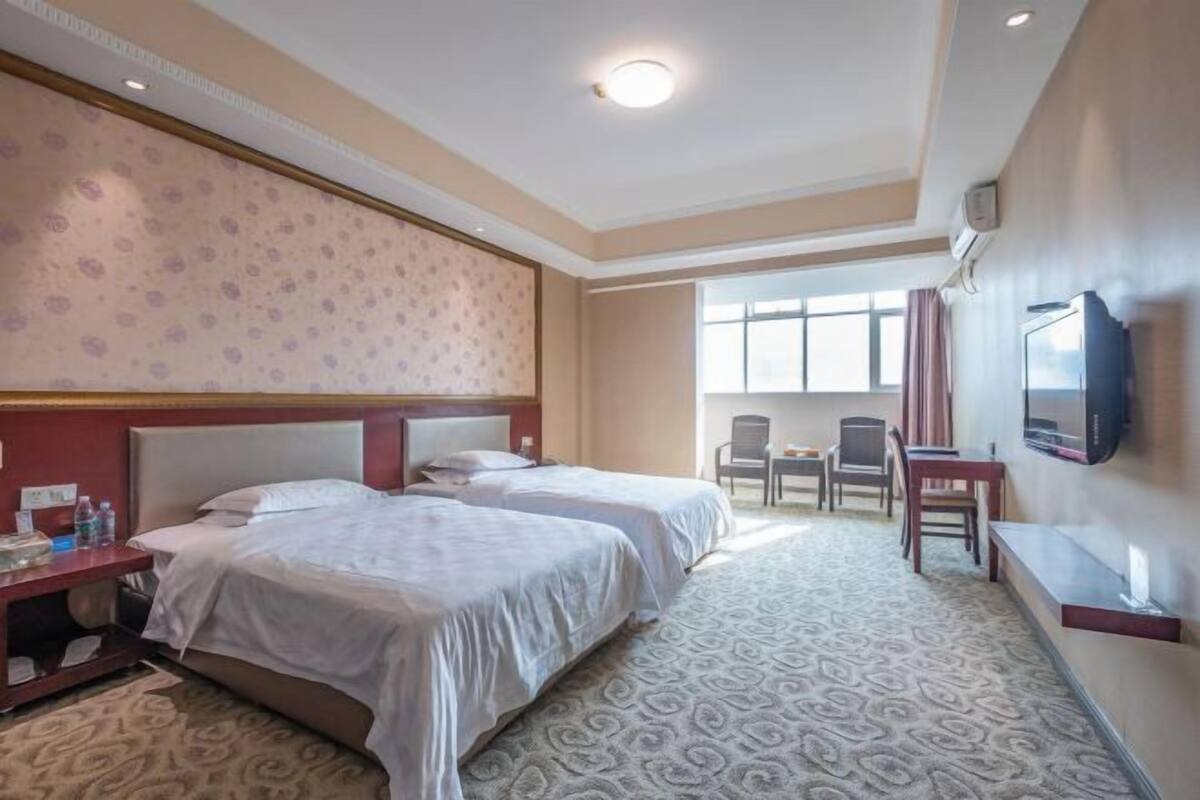 A hotel room with two beds, a TV, a desk, and a window with curtains.