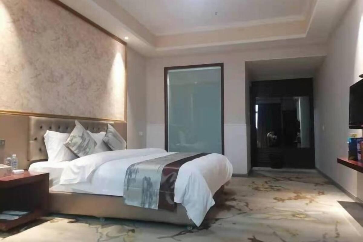 A hotel room with a bed, a nightstand, a TV, and a large window.