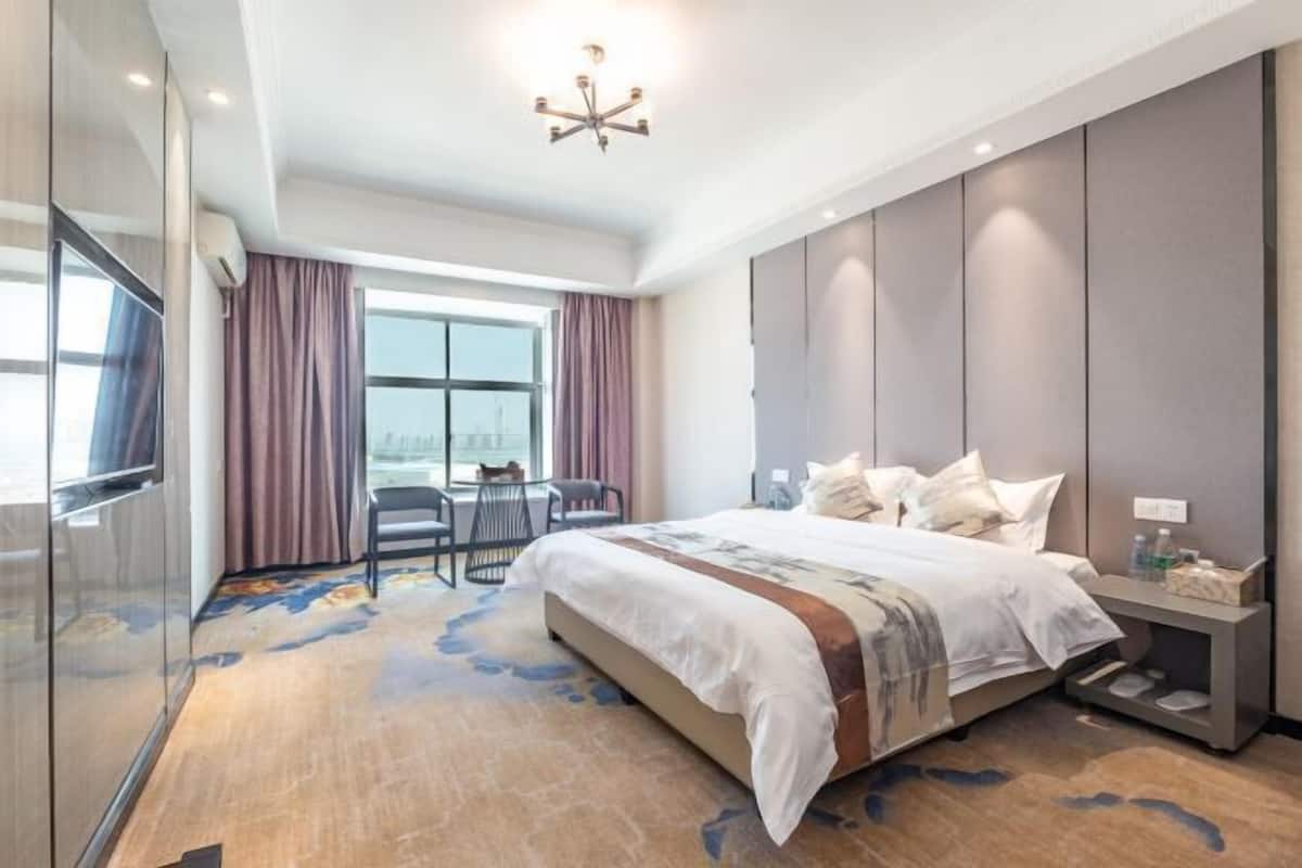A modern hotel room with a large bed, a desk, and a view of the city.