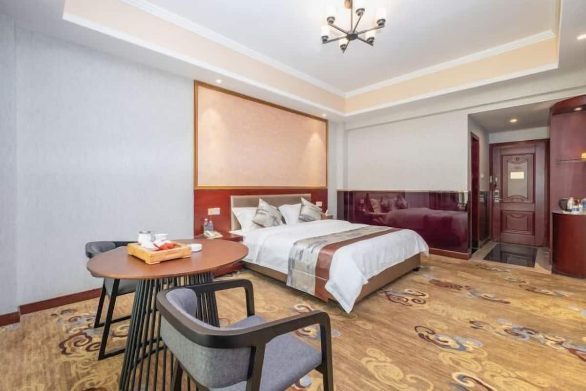 A hotel room with a bed, a desk with a chair, a small table with a tray of items, and a carpeted floor.