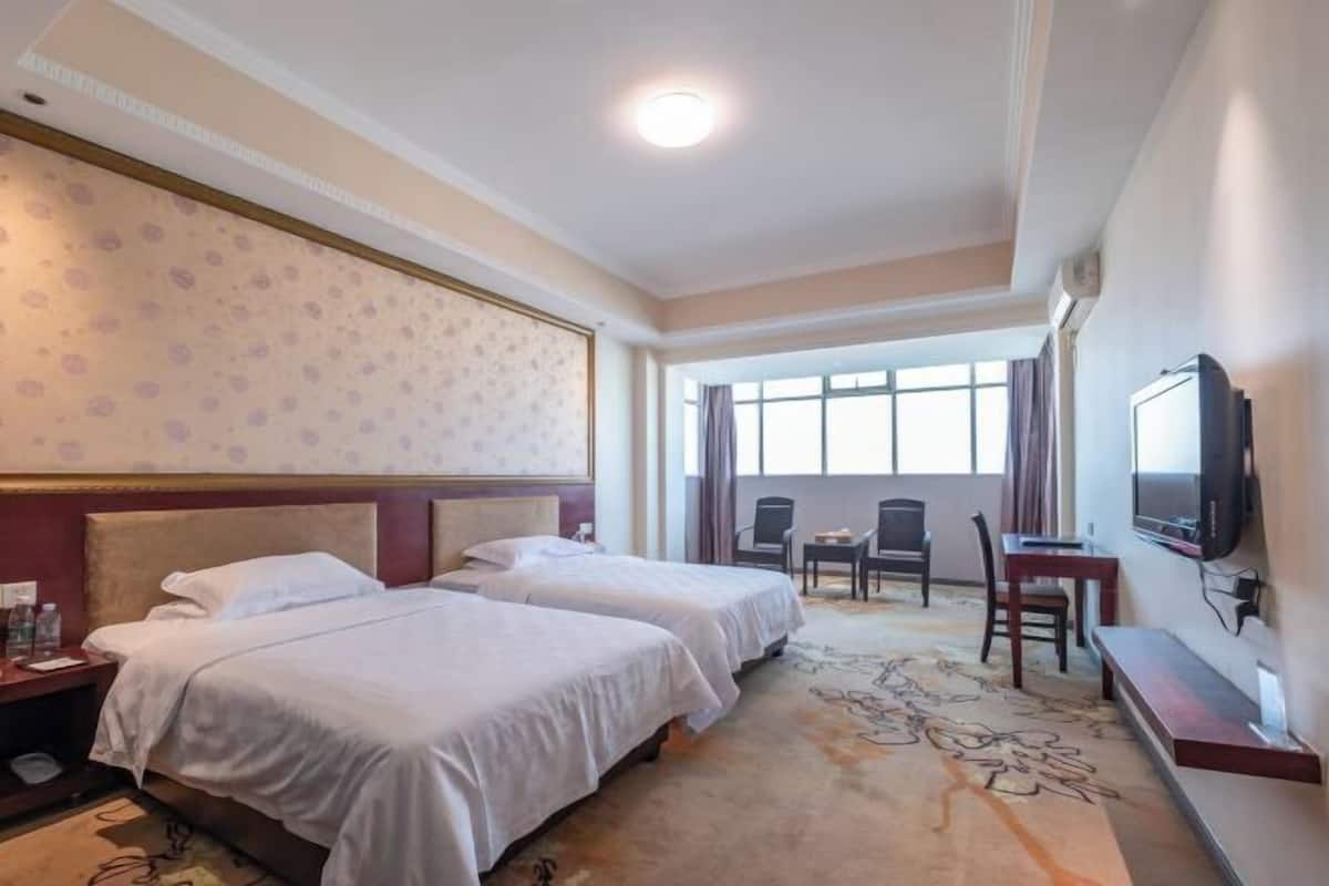 A hotel room with two beds, a TV, a desk, and a large window.