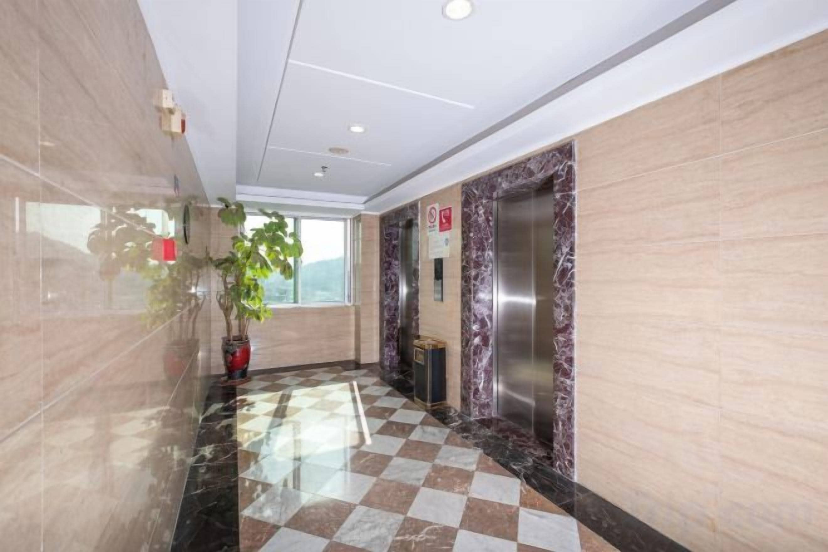 A hotel lobby with a checkered floor, marble walls, an elevator, and a potted plant.