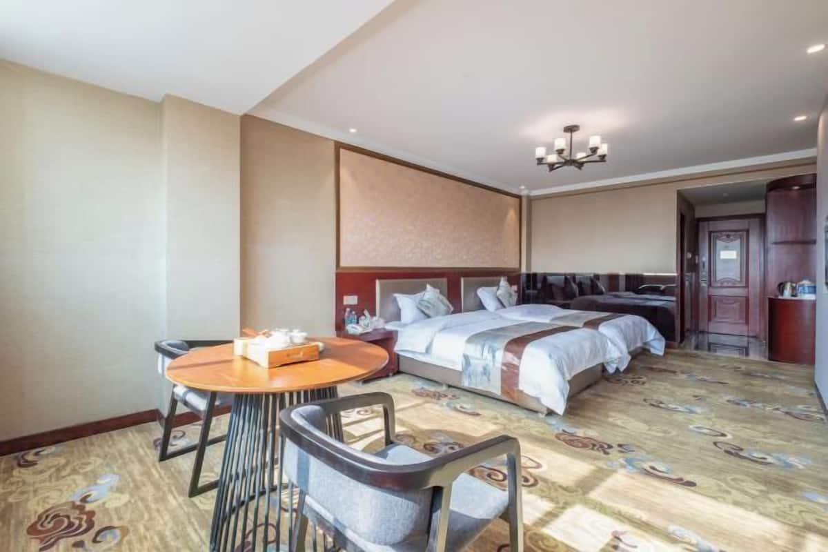 A hotel room with a bed, a dining table with chairs, a chandelier, and a patterned carpet.