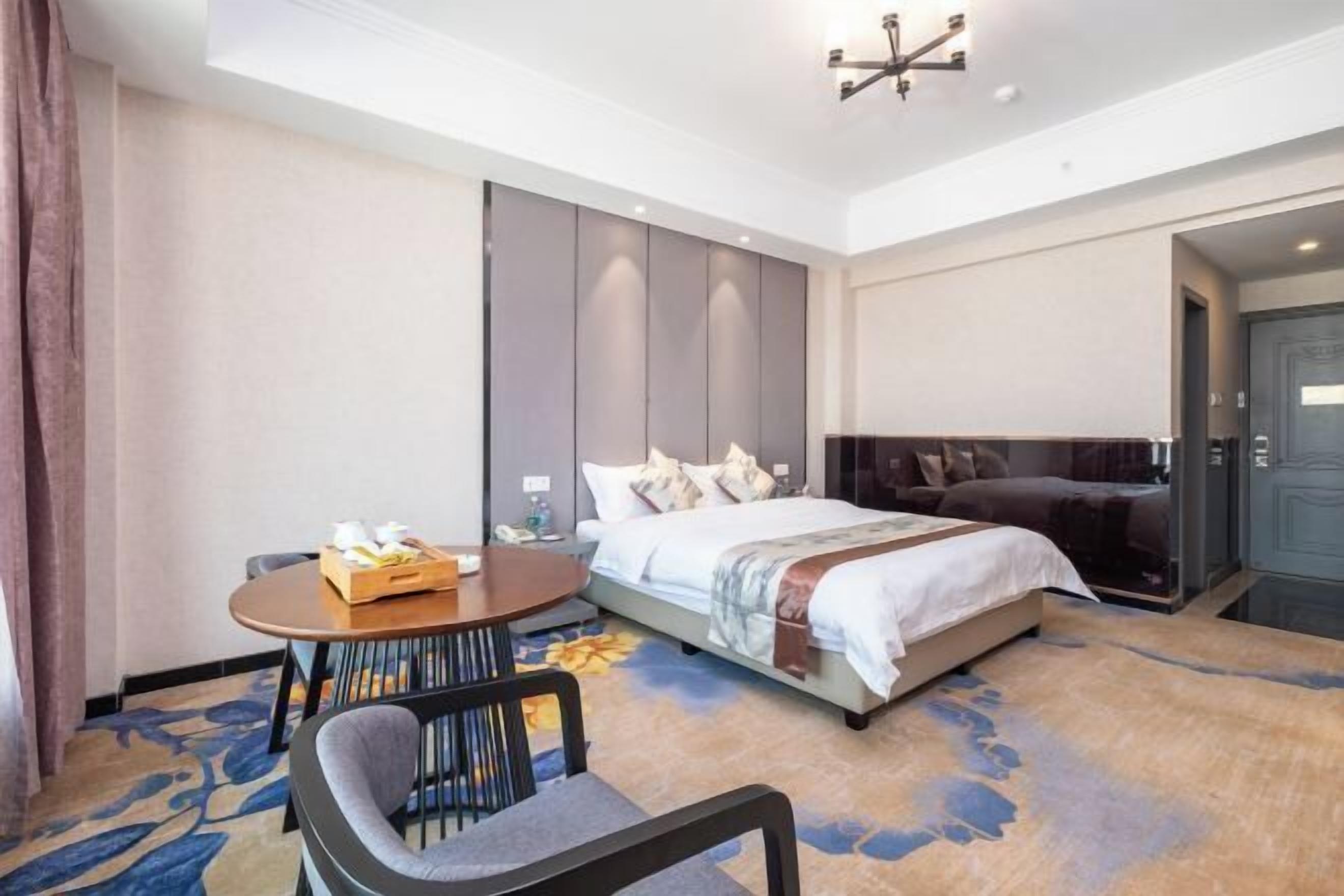 Ein Hotelzimmer mit einem Bett, einem runden Tisch mit Tablett und verschiedenen Gegenständen, einem Stuhl und einem großen Spiegel.