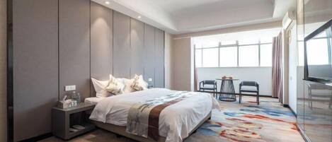 A hotel room with a large bed, a nightstand, a chair, a desk, and a large window.