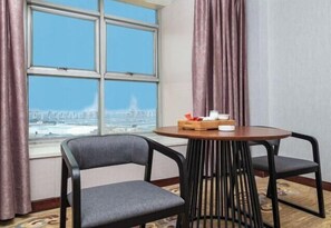 Una habitación con un ventanal grande, dos sillas, una mesita redonda con una bandeja y vistas a un puente.