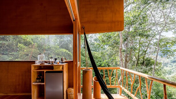 Una terraza de madera con zona de cocina, que incluye un refrigerador y un lavamanos, con vista a un bosque exuberante.