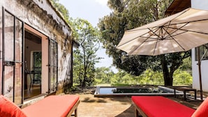 Zona de piscina con dos sillas reclinables rojas, una mesa de madera con dos tazas y un paraguas grande.