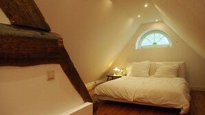 Un dormitorio con techo inclinado, una cama, una mesita de noche, una lámpara y una ventana.