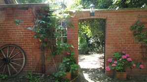 Pared de ladrillo con una rueda de madera, plantas en macetas y un sendero de jardín.