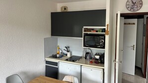 Eine kompakte Küche mit Mikrowelle, Spüle und Geschirrspüler. Eine Uhr ist an der Wand befestigt.