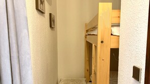 Ein schmaler Flur mit einer hölzernen Bank, einem Etagenbett und einer Wandleuchte.