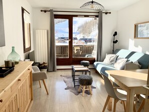 Un salon chaleureux avec une table à manger en bois, un canapé et une vue sur un paysage enneigé par la porte vitrée.