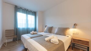 Moderni hotellihuone, jossa on kaksi sänkyä, tuoli, yöpöytä ja ikkuna, jossa on verhot.