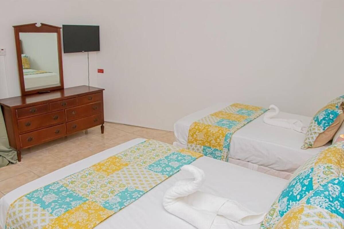 A hotel room with two beds, a wooden dresser, a flat-screen TV, and a patterned bedspread.