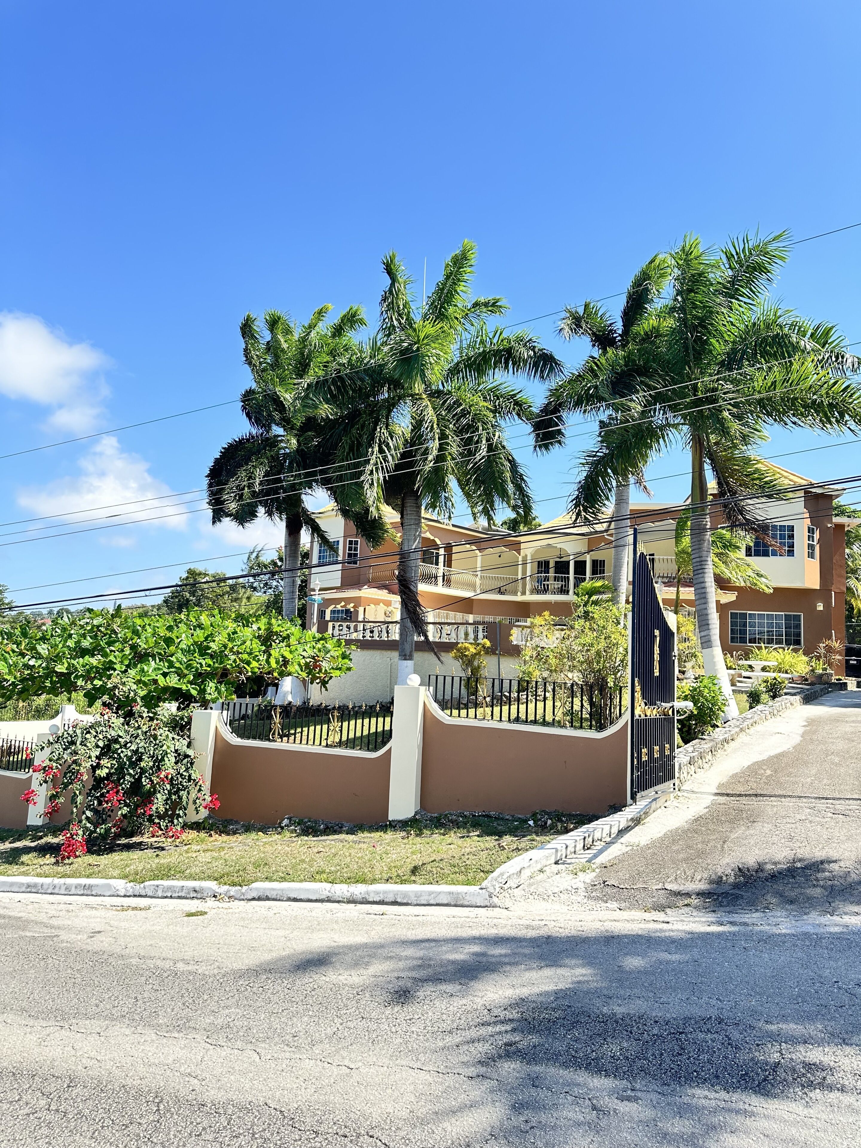 A residential area with palm trees, a gated entrance, and a multi-story building with balconies.