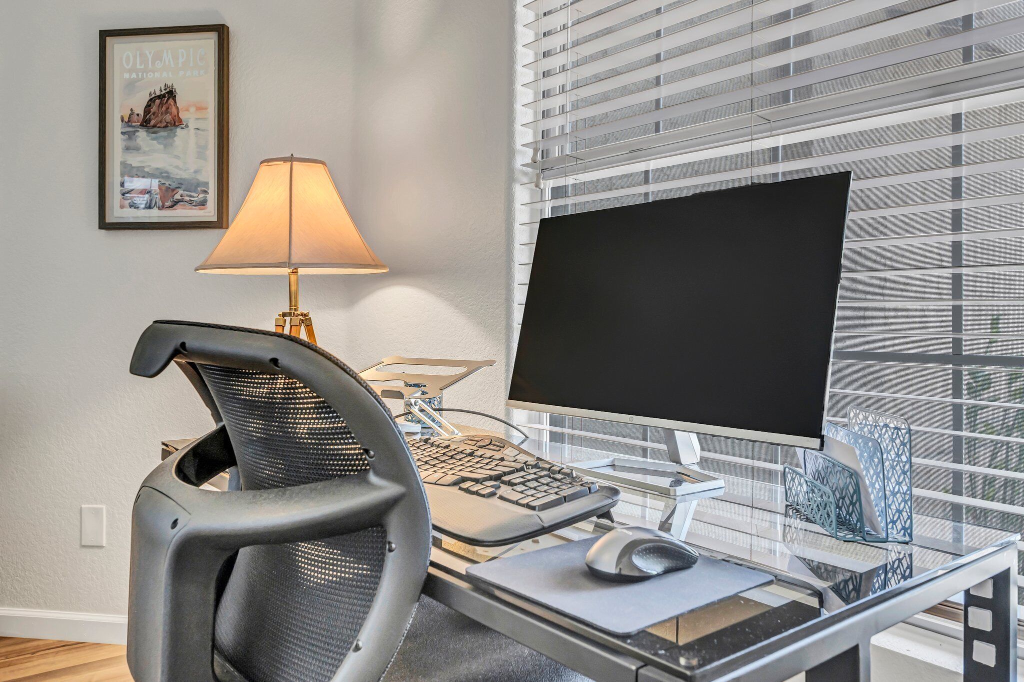 A modern office space with a desk, chair, computer monitor, keyboard, and lamp.