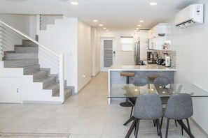 A modern kitchen with a glass dining table and chairs, a staircase, and an air conditioning unit. - 247B South Finger Waterfront Villa, Jolly Harbour (Jolly Harbour)