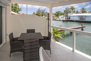 A covered outdoor area with a table and chairs, overlooking a body of water with boats and palm trees. - 247B South Finger Waterfront Villa, Jolly Harbour (Jolly Harbour)