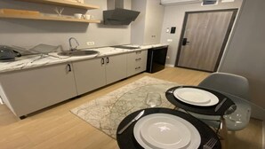Cocina moderna con armarios blancos, horno empotrado y una zona de comedor dispuesta con platos y cubiertos.
