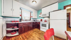 Une cuisine de taille réduite avec des meubles blancs, un four à micro-ondes, une cuisinière et un réfrigérateur.