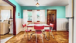 Comedor con mesa de madera y sillas rojas, una ventana con cortinas y una puerta al fondo.