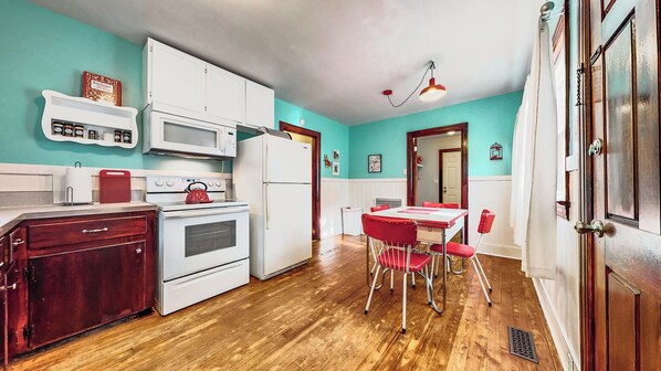 Una cocina con electrodomésticos blancos, un hervidor rojo y una zona de comedor con sillas rojas.