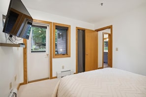 A bedroom with a bed, a TV mounted on the wall, and two doors leading to other rooms.