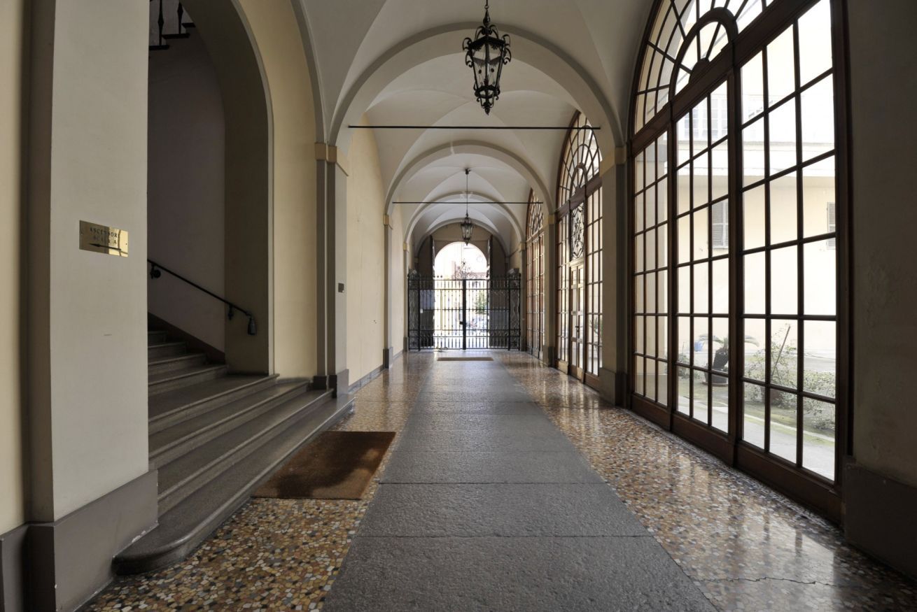 A corridor with a staircase on the left, a large arched window on the right, and a hanging light fixture in the center.