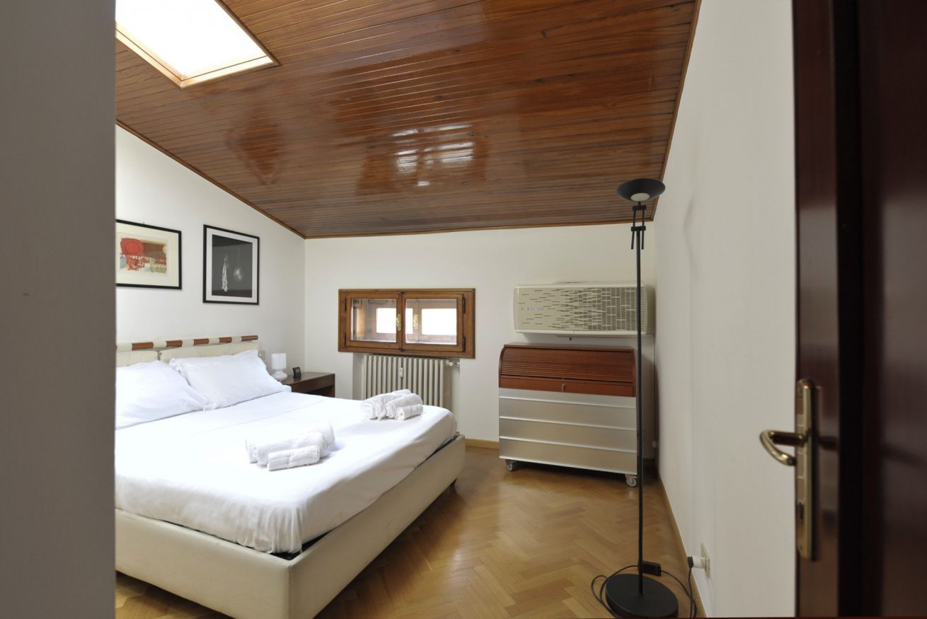 A bedroom with a wooden ceiling, a bed with white linens, a dresser, a radiator, and a window.