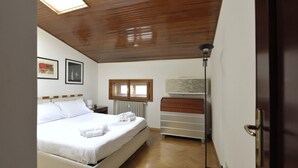 Ein Schlafzimmer mit Holzbalkendecke, einem Bett mit weißer Bettwäsche, einem Schminktisch, einem Heizkörper und einem Fenster.