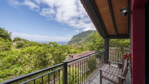 Ein Balkon mit Holzgeländer, der auf eine üppige Landschaft und das Meer in der Ferne blickt.